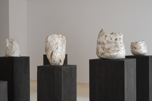 Ceramic sculptures on black pedestals against a plain wall